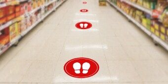 Floor graphics with white footprints in red circles show recommended social distancing in a grocery store aisle.
