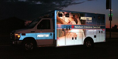 An emergency vehicle at night wrapped in a shining, reflective 3m graphic wrap with the words newborn intensive care unit on the side of the vehicle.
