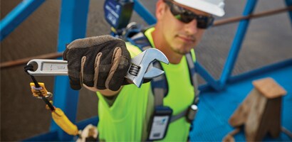 Image of worker holding an adjustable wrench secured to his belt by a tether
