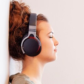 女士倚牆而立，用無線頭戴式耳機聆聽音樂