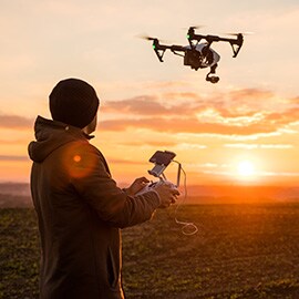 男子戶外操作雙手遙控器，控制空中的攝像無人機