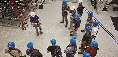 Group of wokers in safety gear gathered around fall protection instructor
