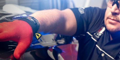 An installer smooths a car wrap with his gloved hand.
