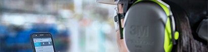 worker wearing earmuffs looking at his phone
