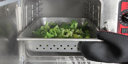 Broccoli in an oven tray in an oven being steamed

