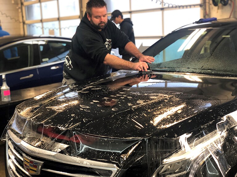man applying 3M paint protection film to the hood of a black car
