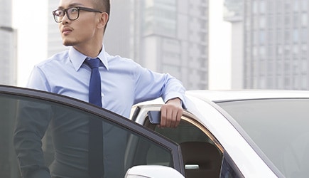 A professional-looking man stands behind an open car door, showing how the window tint creates a soft gray hue.