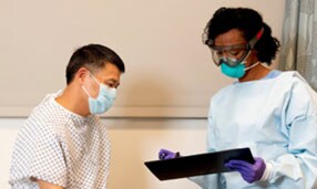 Clinician wearing PPE speaking with a patient
