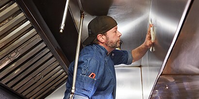 Man on a ladder safely using a degreaser wipe
