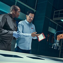 two experts in a factory discuss smart device screens which are laid out before them.