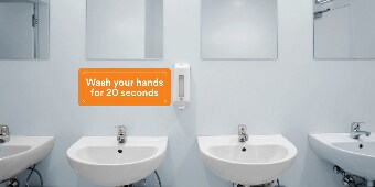An orange wall graphic above the sinks in a public restroom reads “Wash your hands for 20 seconds.”
