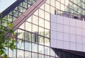 3M™ Sun Control Window Films seen from the exterior of a building reflect light and nearby trees.