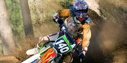A motocross racer with a helmet on a motorcycle kicking up dirt on a curve, and  wrapped in a 3m personal recreational vehicle wrap with flames on the front.
