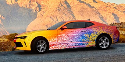 A sports car driving on a highway in the canyons, wrapped in a yellow to blue to orange fade 3M 780mC graphic wrap.