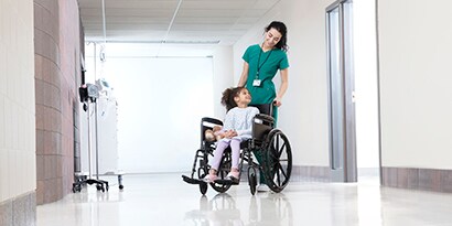 female health care professional pushing a young patient in a wheelchair
